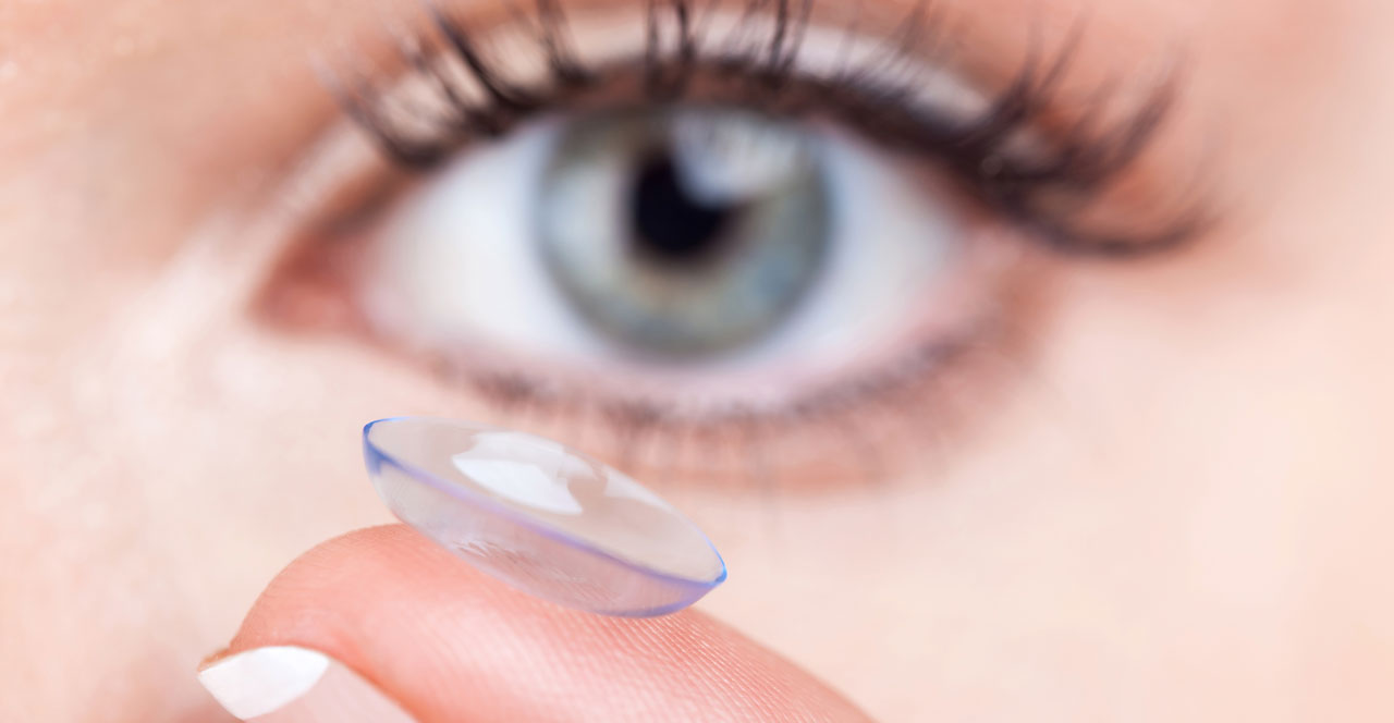 close up of woman's eye and a contact lens on her fingertip
